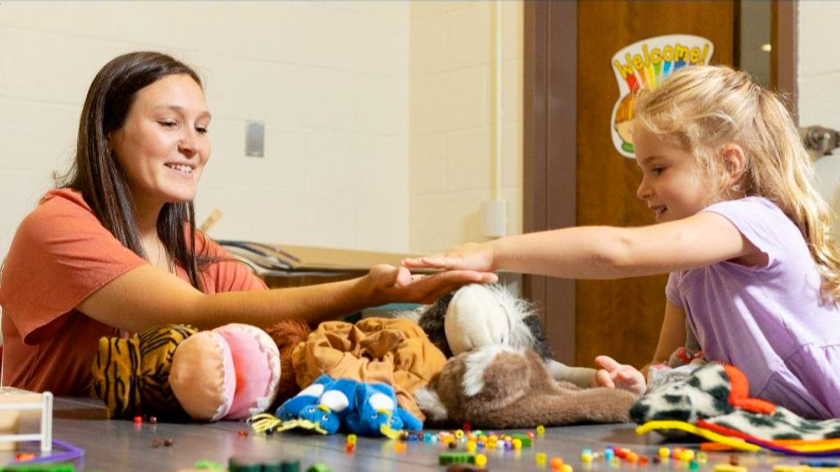 Photo of student-teacher interacting with a young child in a classroom.